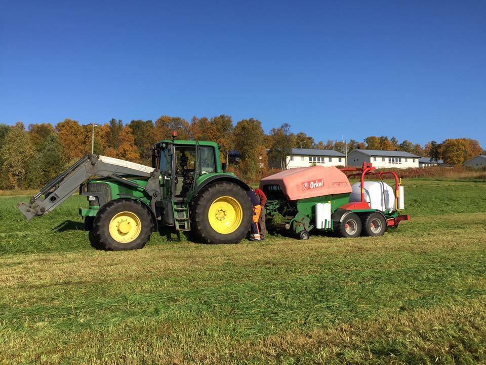 En traktor trekker landbruksmaskin som lager innpakkete høyballer - Klikk for stort bilde
