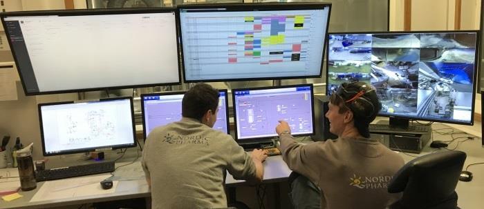 Bilde av et kontrollrom med mange skjermer som to elever følger med på - Klikk for stort bilde