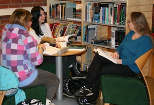 Lærer Larissa Johansen sitter sammen med to elever og diskuterer fag i skolens bibliotek. - Klikk for stort bilde
